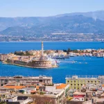 The Strait of Messina between Sicily and Italy. View from Messina town with golden statue of Madonna della Lettera and entrance to harbour. Calabria coastline in background