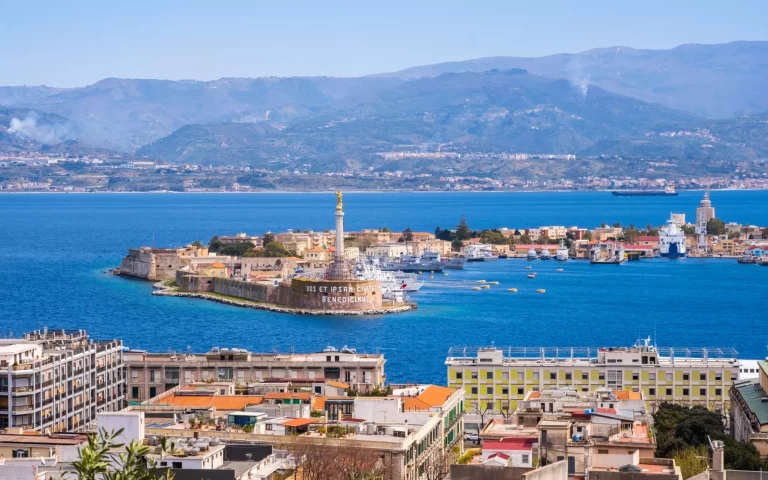 The Strait of Messina between Sicily and Italy. View from Messina town with golden statue of Madonna della Lettera and entrance to harbour. Calabria coastline in background