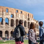 Three happy young friends tourists in front of colosseum in rome