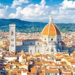 Top aerial panoramic view of Florence city with Duomo Cattedrale di Santa Maria del Fiore cathedral, buildings houses with orange red tiled roofs and hills range, blue sky white clouds, Tuscany, Italy