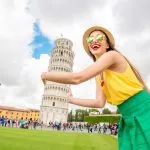 Young female traveler having fun in front of the famous leaning tower in Pisa old town in Italy. Happy vacations in Italy