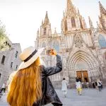 Young woman tourist photographing with phone famous saint Eulalia church during the morning light in Barcelona city